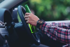 Zoom em mão de motorista segurando garrafa de cerveja enquanto ao volante