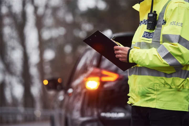 Policial com uniforme verde em pé com o bloco de notas perto do carro.