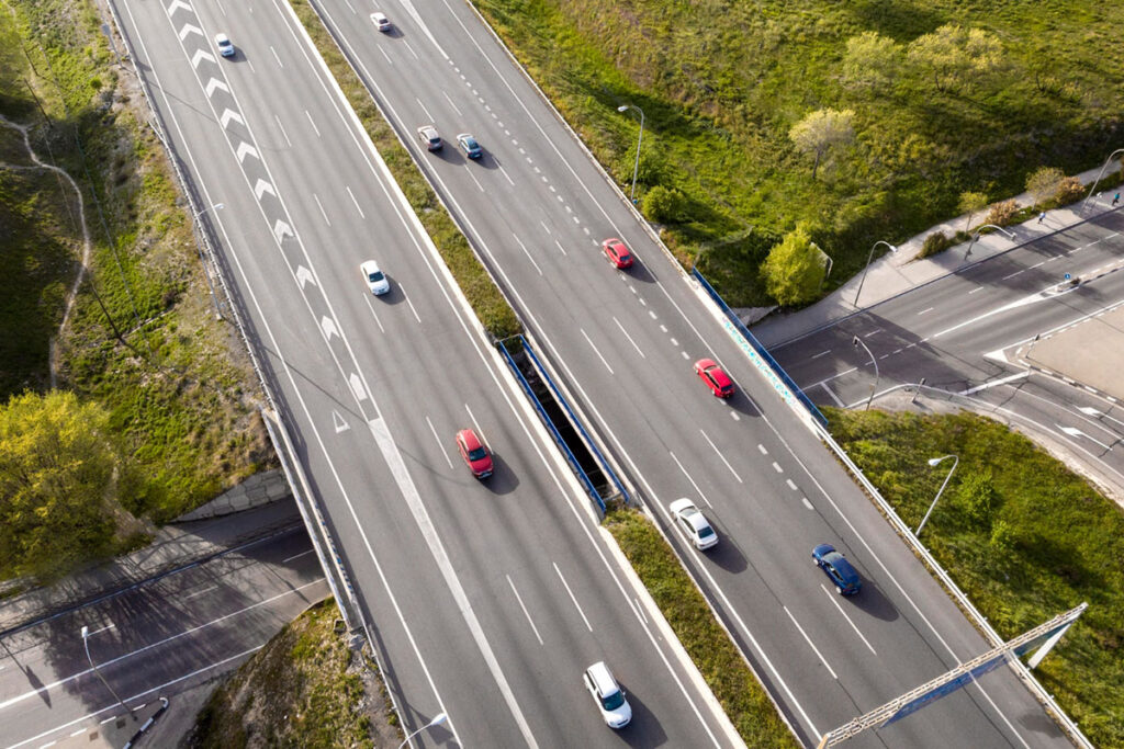 Vista superior de avenida com seis pistas, de sentido duplo, com veículos circulando