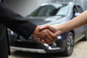 Homem e mulher apertam as mãos com carros ao fundo.