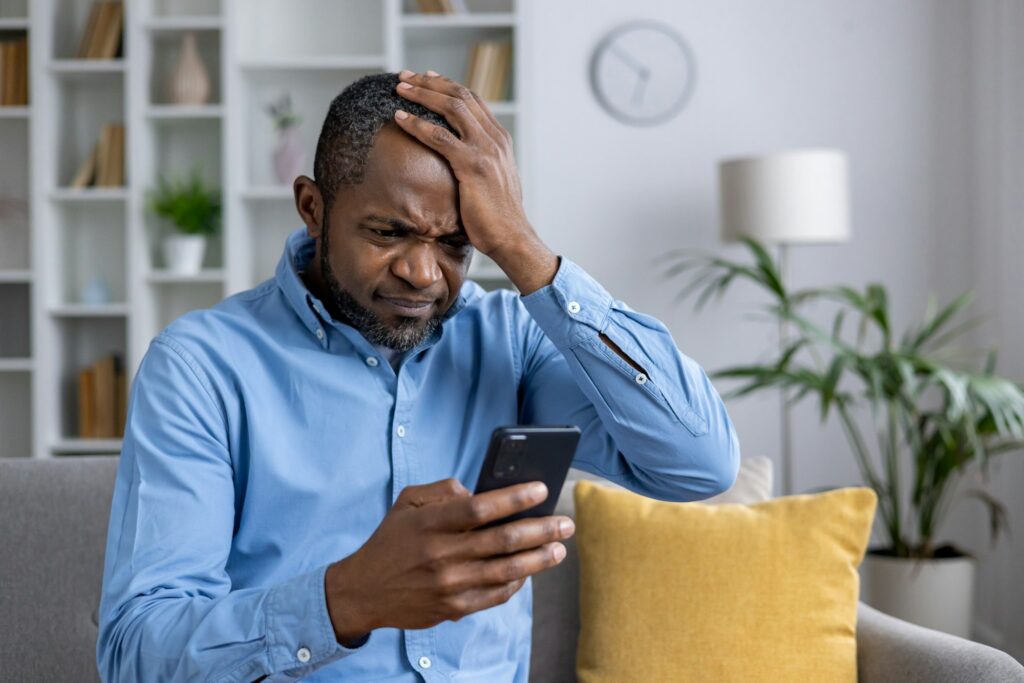 Homem negro preocupado e tenso ao olhar para a tela de seu celular