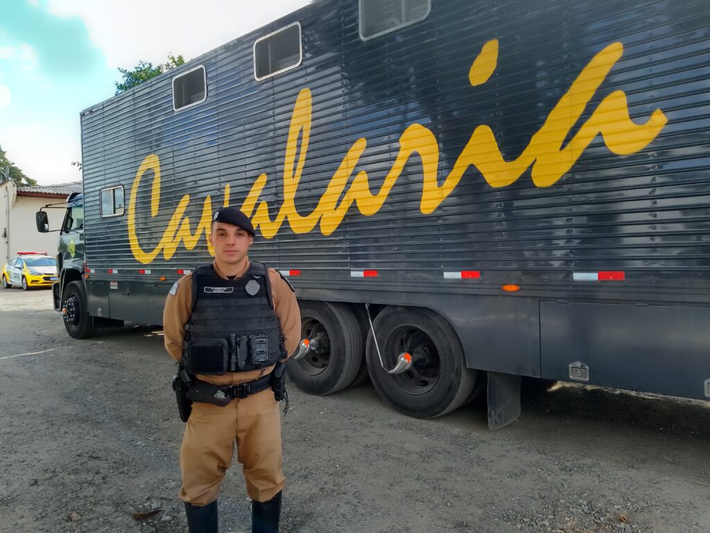 2º tenente do Regimento posa para foto com o caminhão de carga viva atrás. No veículo, aparece em amarelo a palavra "cavalaria". 