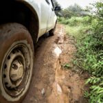 Foto em detalhe mostra estrada de terra lamacenta próxima ao pneu de veículo